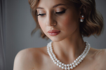 Portrait of happy elegant young woman in modern bridal look with classic hairstyle and makeup with pearl necklace