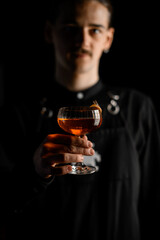 Bartender holding a glass full of cocktail by the stem in front of him