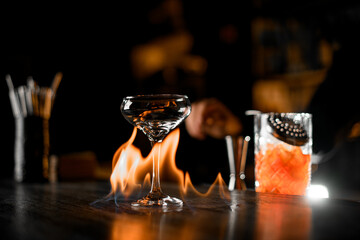 Hands of a bartender pouring a cocktail from a mixing glass, straining it through a sieve into a...