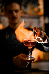 Focus on flaming cocktail glass that bartender holds in front of him and sprays it