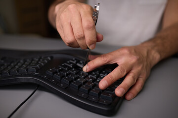 In a closeup shot, a hand is seen using a keycap puller tool to meticulously remove a keyboard key