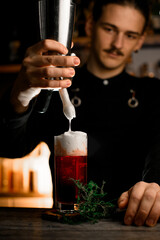 Bartender has added foam to a cocktail glass with a frother