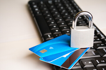 A padlock over a pair of credit cards next to a computer keyboard on a white background with copy space


