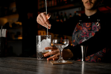Bartender stirs a cocktail with crushed ice in a mixing glass with a bar spoon