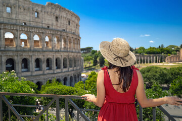 Brunette girl with straw hat admires the majesty of the Colosseum and in the background the ancient...