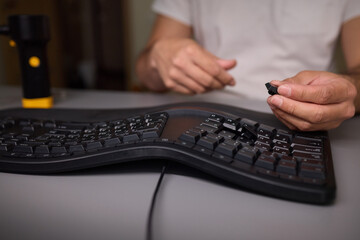 In a closeup shot, a hand is seen using a keycap puller tool to meticulously remove a keyboard key