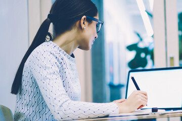 Back view of female student reading information from web page browsed on laptp computer with blank...