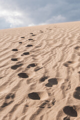 Footprints of a person on the dunes that lead to somewhere on the beach. Concept: path, follow