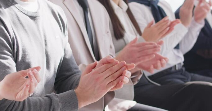 Audience applauding at a business convention, work conference or educational seminar. Crop shot of people in smart casual wear and formal suits sitting in a row and clapping their hands