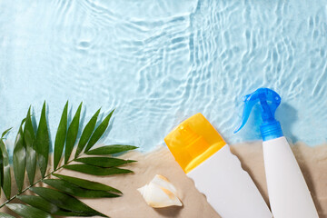 Sunscreen bottles and a palm leaf on a sandy beach with water ripples, perfect for a summer...