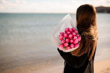 Turned away girl in black clothing standing near a water with a beautiful pink flowers