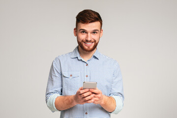 Young bearded man using his phone and smiling on studio background, websurfing or scrolling, copy...
