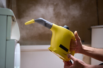 hand in gloves. Using a steam cleaner to clean a washing machine