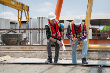 Engineer or architect with a hardhat examines the schedule on a set of plans. Two businessmen, both engineers, at the construction site.