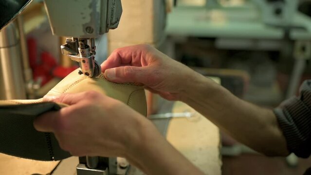 Male bootmaker is sewing fabrics for shoes in shoe workshop. Shoe making process