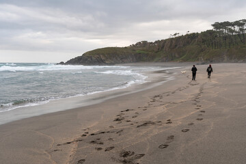 Couple walking with the dog on Frejulfe Beach. Council of Navia, Asturias