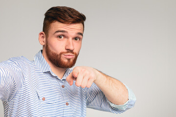 You are cool. Young bearded guy making selfie and pointing you with finger against grey studio...