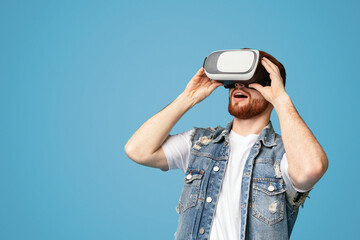 Excited young redhaired man enjoying virtual reality glasses experience, modern entertainment, blue...