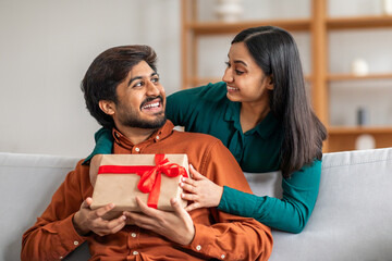 A smiling Indian couple enjoys a moment together as one presents a beautifully wrapped gift with a...
