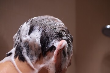 Man washing hair with shampoo in shower, creating foamy lather - personal hygiene care.