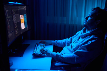 A coder is working late at night on a computer screen, coding and using a smartphone app