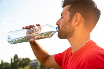 man drinking water outdoors after sports