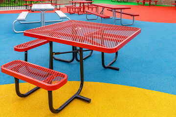 Red vinyl coated ADA, wheelchair, accessible picnic table  on a multi color playground surface.	