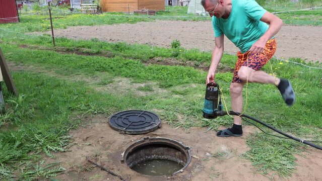 Homeowner lowers submersible wastewater pump into septic tank maintenance hole.