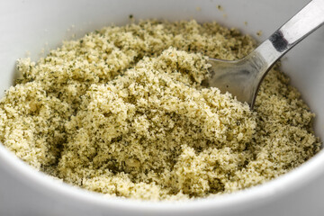 Ground crushed pumpkin seeds as a raw ingredient for dietary pastry in white kitchen cup with spoon