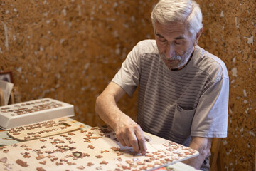 Dementia prevention. Elderly man hands doing jigsaw puzzle at home