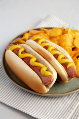 Homemade Hot Dog with Mustard and Potato Chips on a Plate, side view.