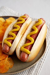 Homemade Hot Dog with Mustard and Potato Chips on a Plate, side view.