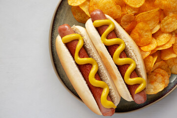 Homemade Hot Dog with Mustard and Potato Chips on a Plate, top view. Copy space.