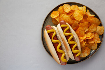 Homemade Hot Dog with Mustard and Potato Chips on a Plate, top view. Copy space.