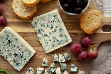 Organic Blue Cheese with Grapes and Olives on a Wooden Board, top view.