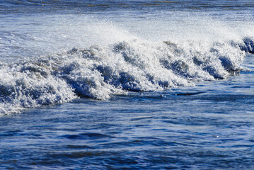 Sea waves forming white foam on sunny day.