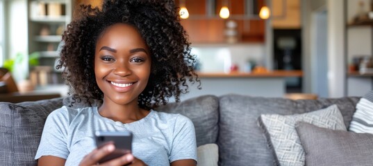 Happy woman with curly hair using smartphone while sitting comfortably on the couch at home