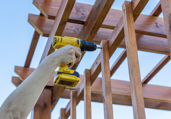 A person is using a drill to attach a wooden fence. The individual is focused on securing the fence...