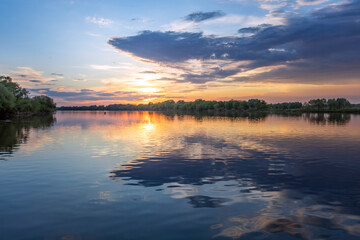 Fototapeta premium The sun, nestled among cotton candy clouds, dips below the horizon, casting gentle hues of orange and pink across the tranquil waters.