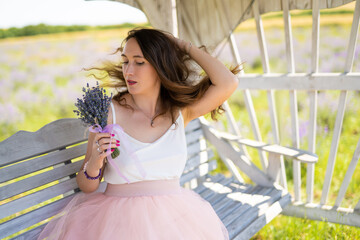 Fototapeta premium a beautiful girl in a dress with a bouquet of lavender flowers sits on a bench