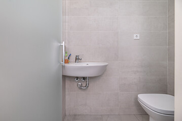 Bathroom with translucent glass door, white porcelain toilets, large gray tiles and frameless mirror on the wall