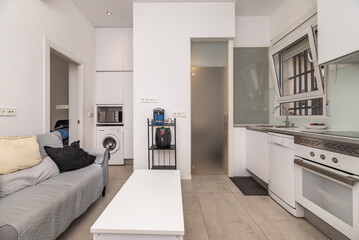 Living room of a typical home with a small kitchen with white furniture and bars on the windows 2