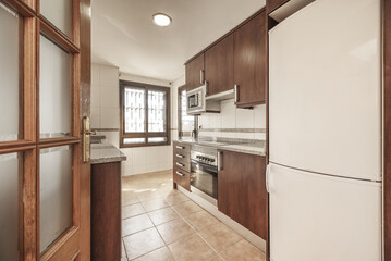 A kitchen with brown wooden furniture, with integrated appliances, gray granite countertops and...
