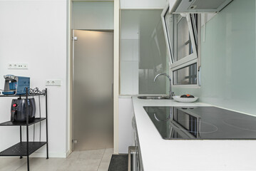 Small kitchen of a loft apartment with white furniture and tempered glass doors and windows