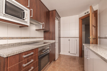 A kitchen with brown wooden cabinets, with integrated appliances, gray granite worktops and sapelly wood doors