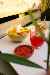 Cocktails with nachos with cream and spicy tomato pepper sauce at beach bar in summer