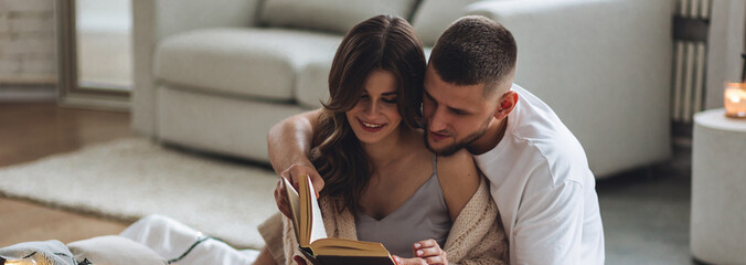 Banner. Beautiful young loving couple having breakfast, drinking hot chocolate or coffee with marshmallow in bed at home. Happy spouses enjoying lazy romantic winter morning in bedroom. Candles - Powered by Adobe