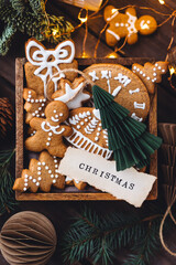 Wooden vintage box with homemade delicious gingerbread cookies decorated with white icing. Cozy home atmosphere, fairy lights, fir tree branches. Handmade zero waste gift for Christmas or New Year