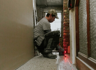 A young man measures brickwork using a laser level.