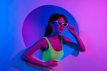 Photo of woman touch sunglass look empty space from circle hole isolated glowing neon background